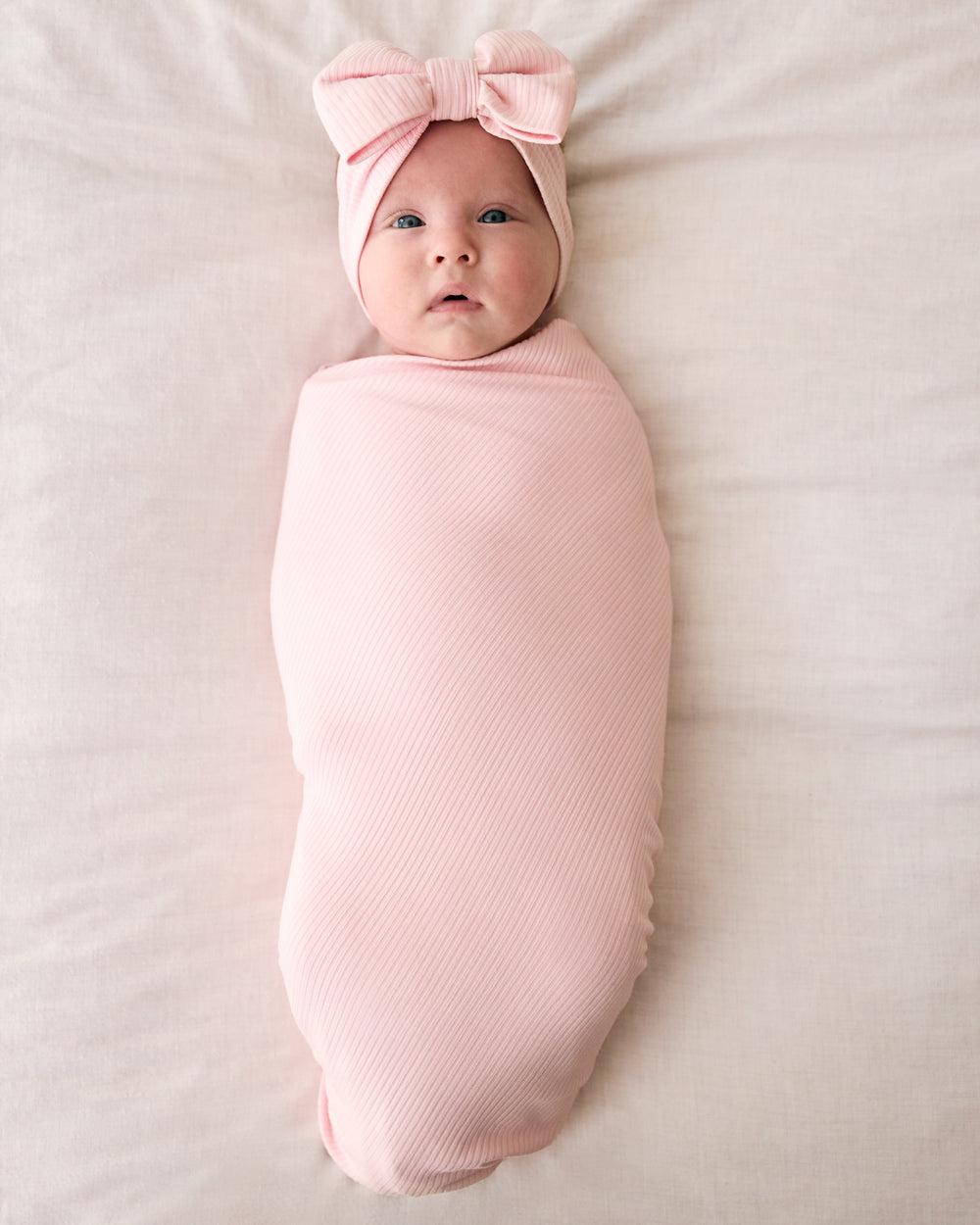 Aerial view of newborn wearing the Prima Pink Ribbed Swaddle & Luxe Bow Headband Set