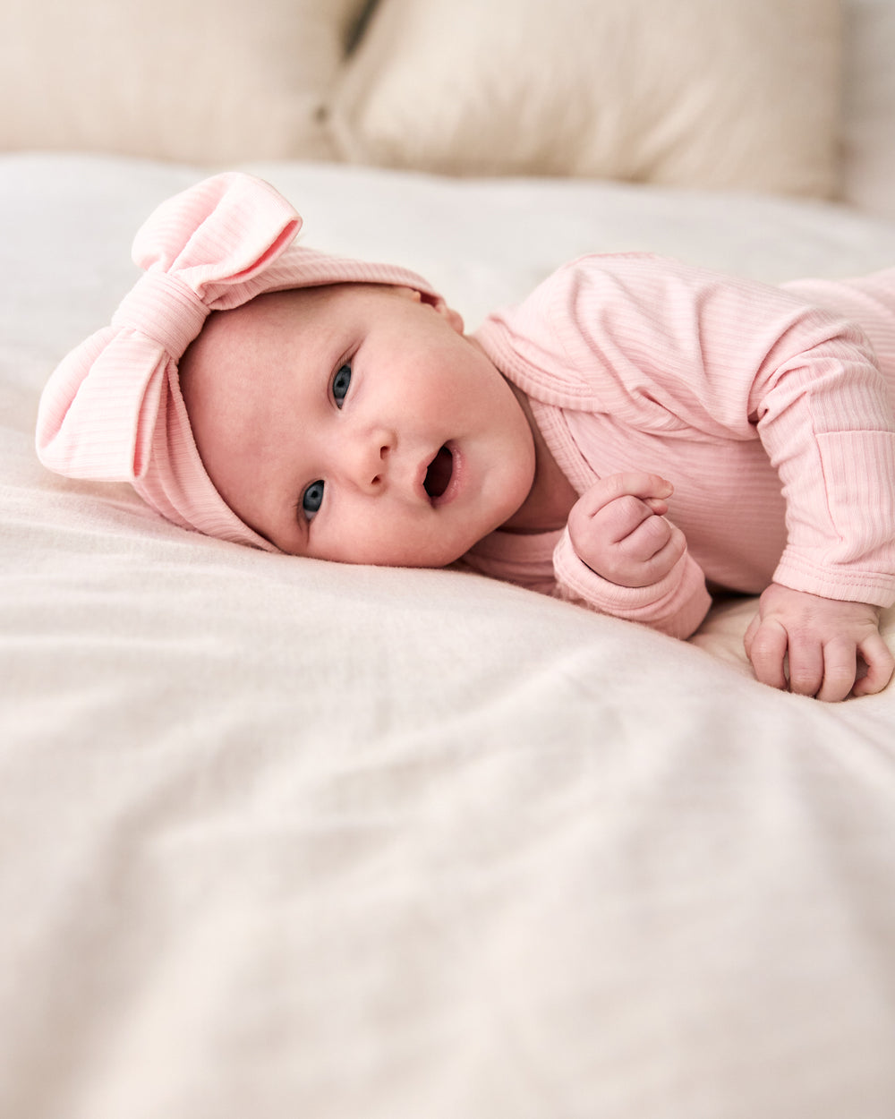 Newborn on a white bed wearing the Prima Pink Ribbed Luxe Bow Headband