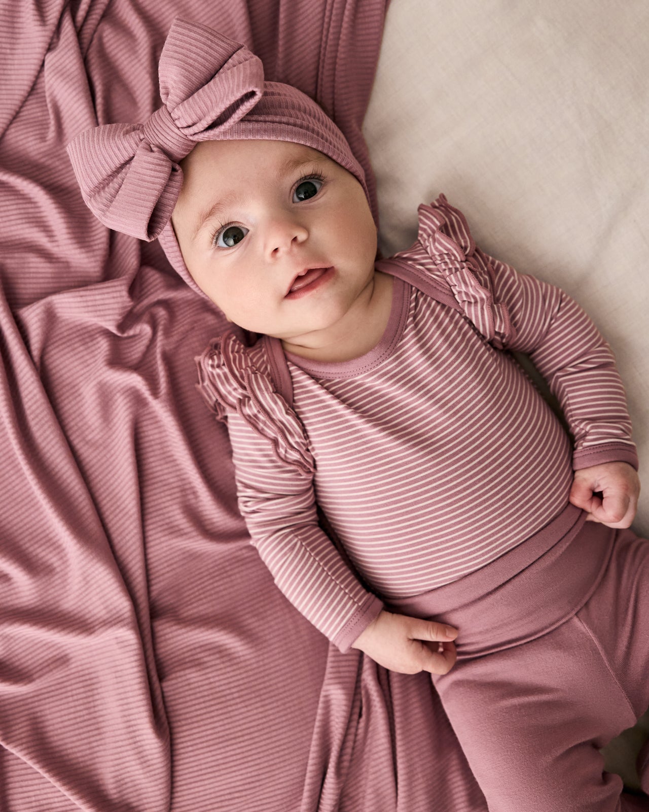 Aerial view of newborn wearing the Rosewood Stripe Flutter Bodysuit with a matching luxe bow headband