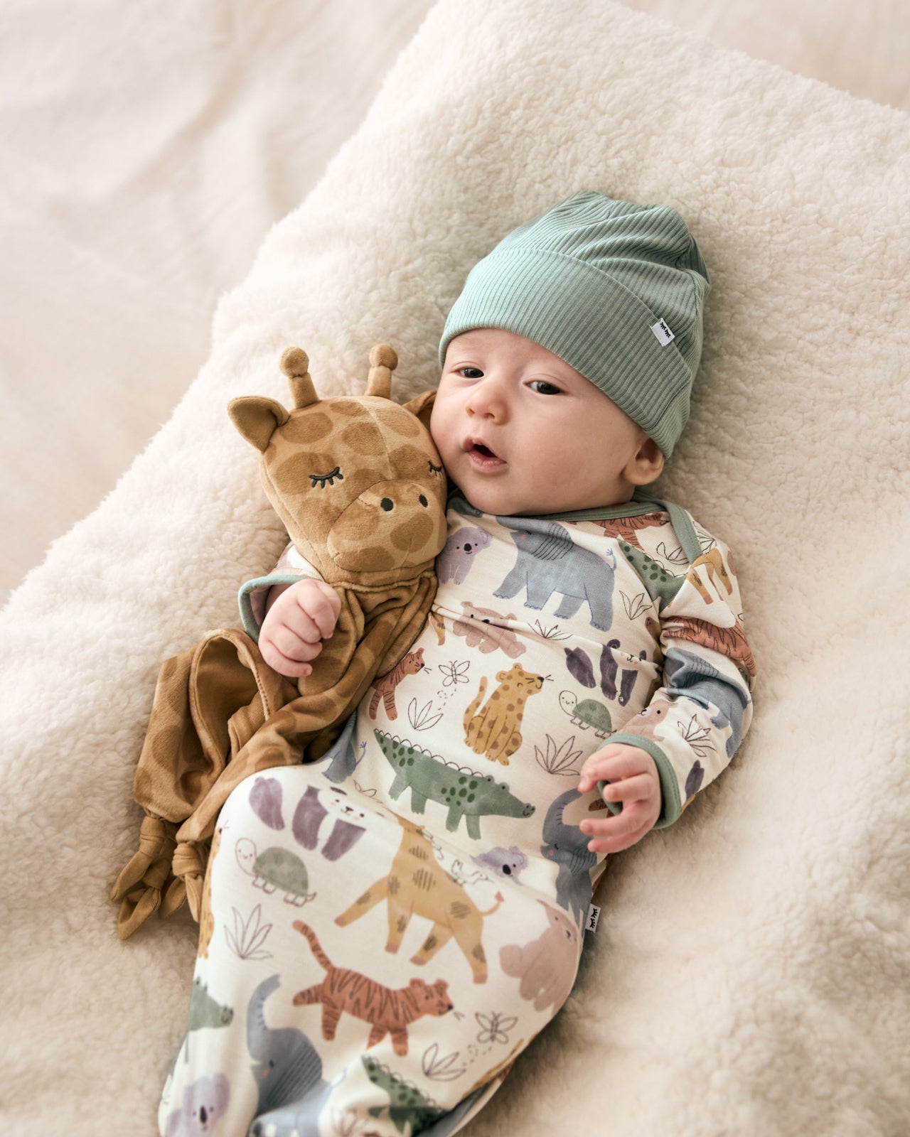 Baby cuddled with the Giraffe Sleepyhead Lovey wearing a safari themed infant gown