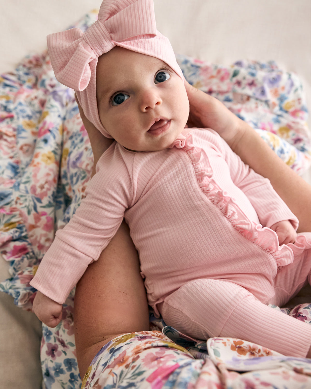 Newborn in mothers arms wearing the Prima Pink Ribbed Ruffle Zippy with a matching pink bow headband