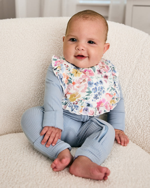 Newborn wearing the Tiny Blooms Ruffle Bib with blue ribbed zipper pajamas