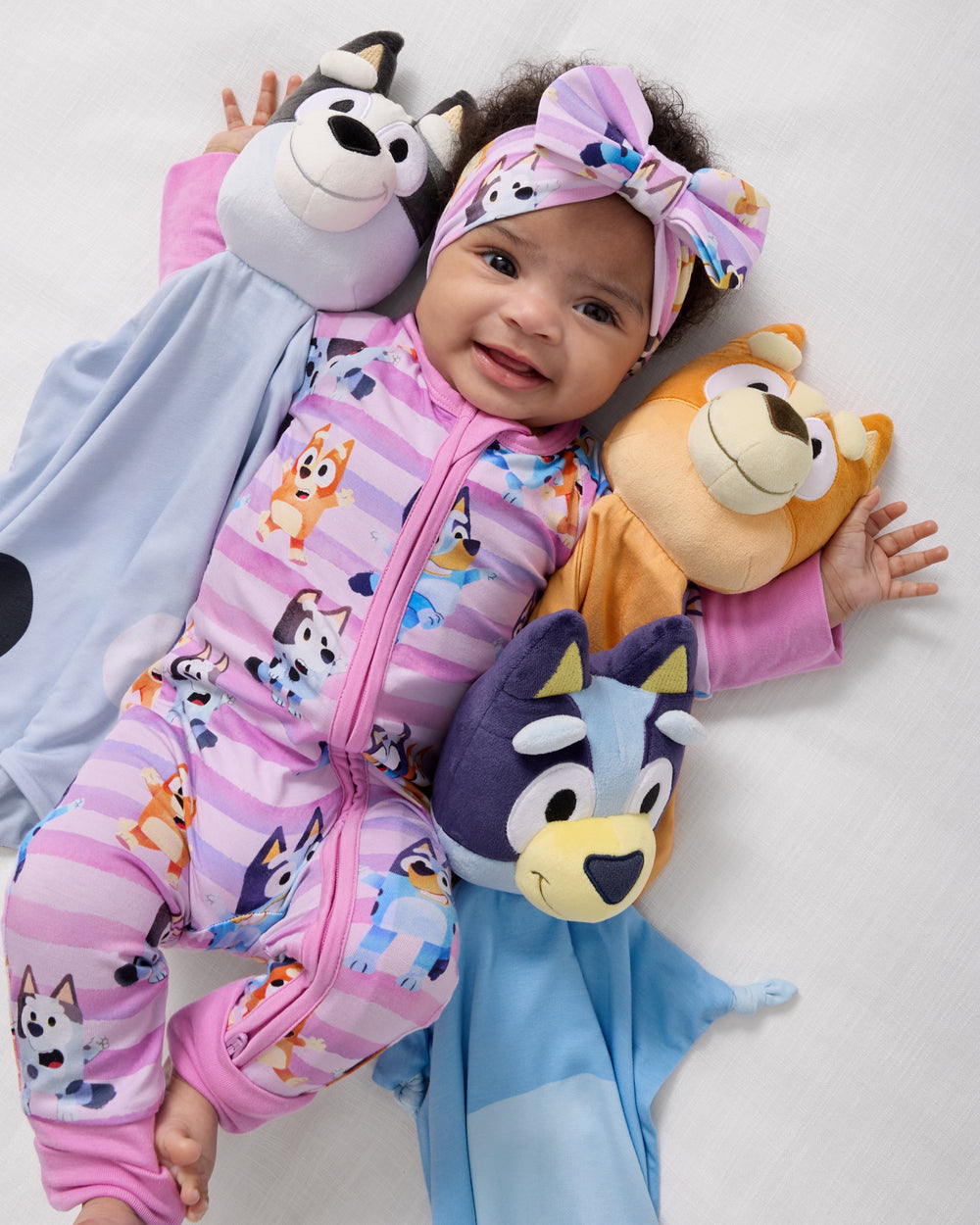 Baby laying with the Bluey, Bingo and Muffin Lovies wearing Bluey baby pajamas