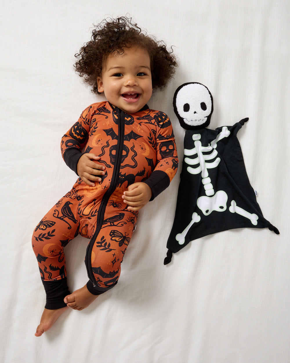 Aerial view of baby laying with the Skeleton Sleepyhead Lovey wearing Halloween footie pajamas