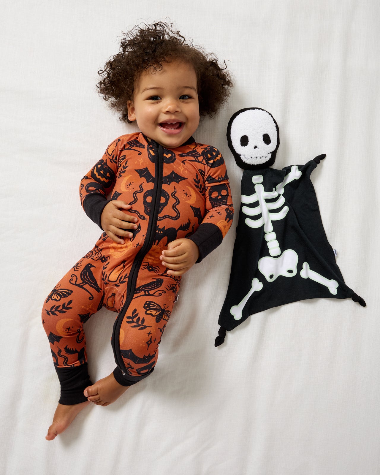 Aerial view of baby laying with the Skeleton Sleepyhead Lovey wearing Halloween footie pajamas