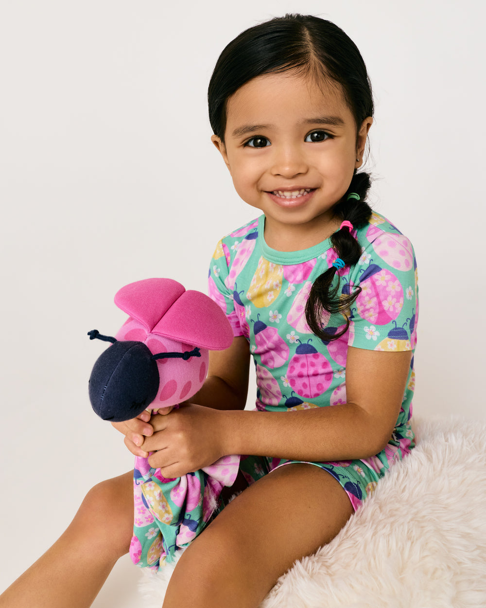 Girl holding the Rosie the Ladybug Sleepyhead Lovey wearing matching ladybug print pajamas