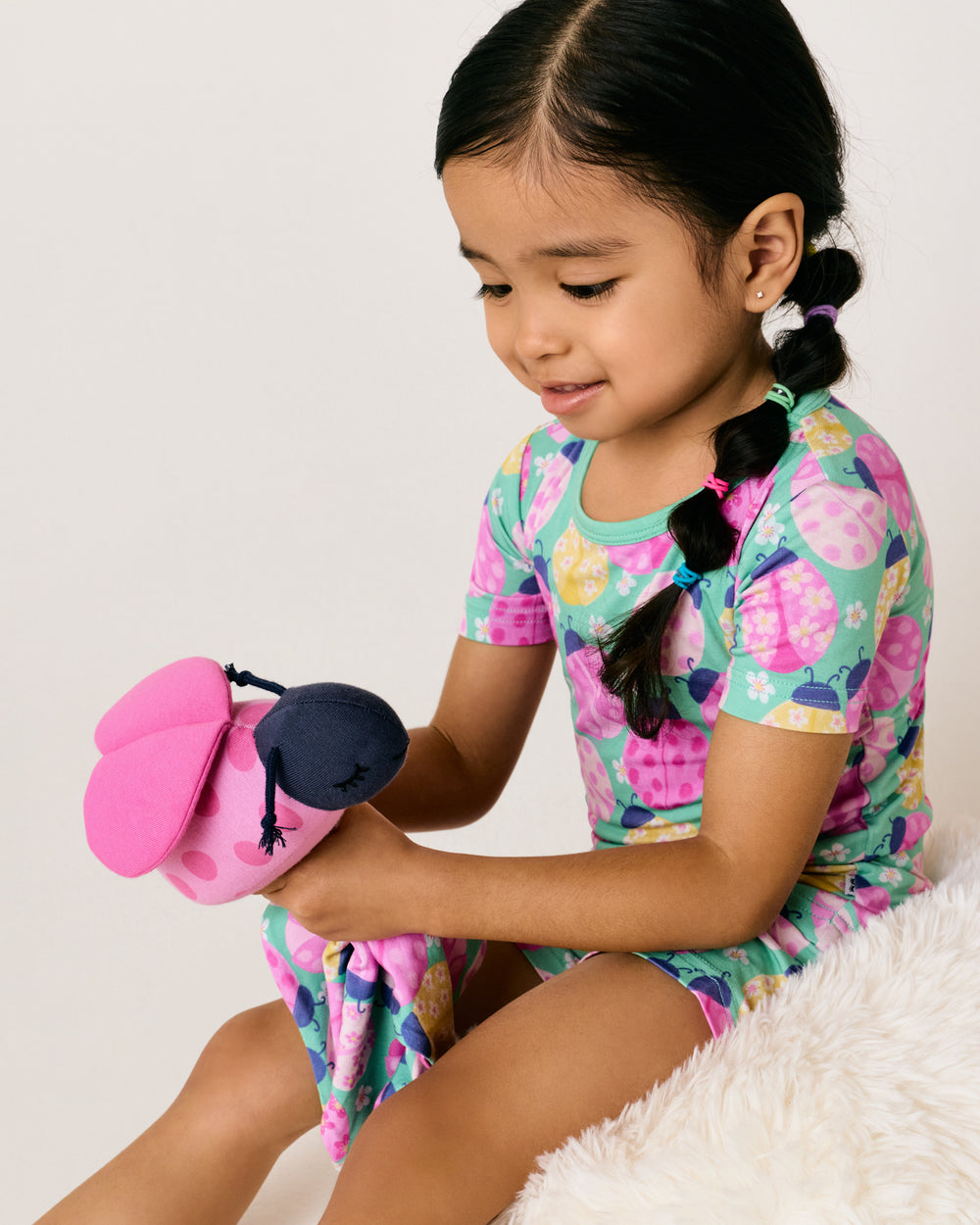 Child wearing the Ladybug Meadow Two-Piece Short Sleeve & Shorts Pajama Set holding the matching plush toy
