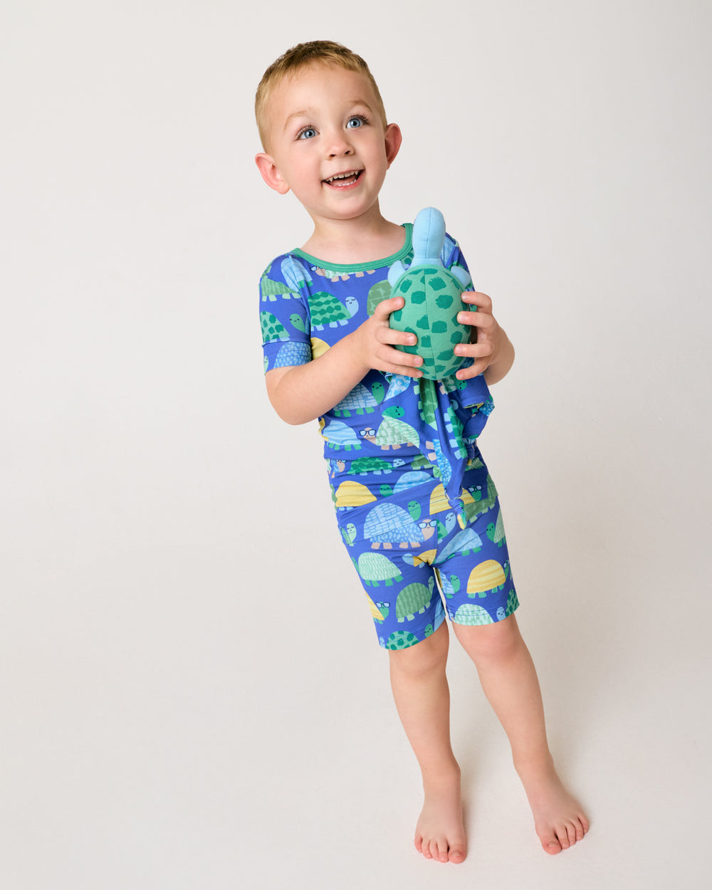 Standing child holding the Ty the Turtle Sleepyhead Lovey wearing the matching pajama set