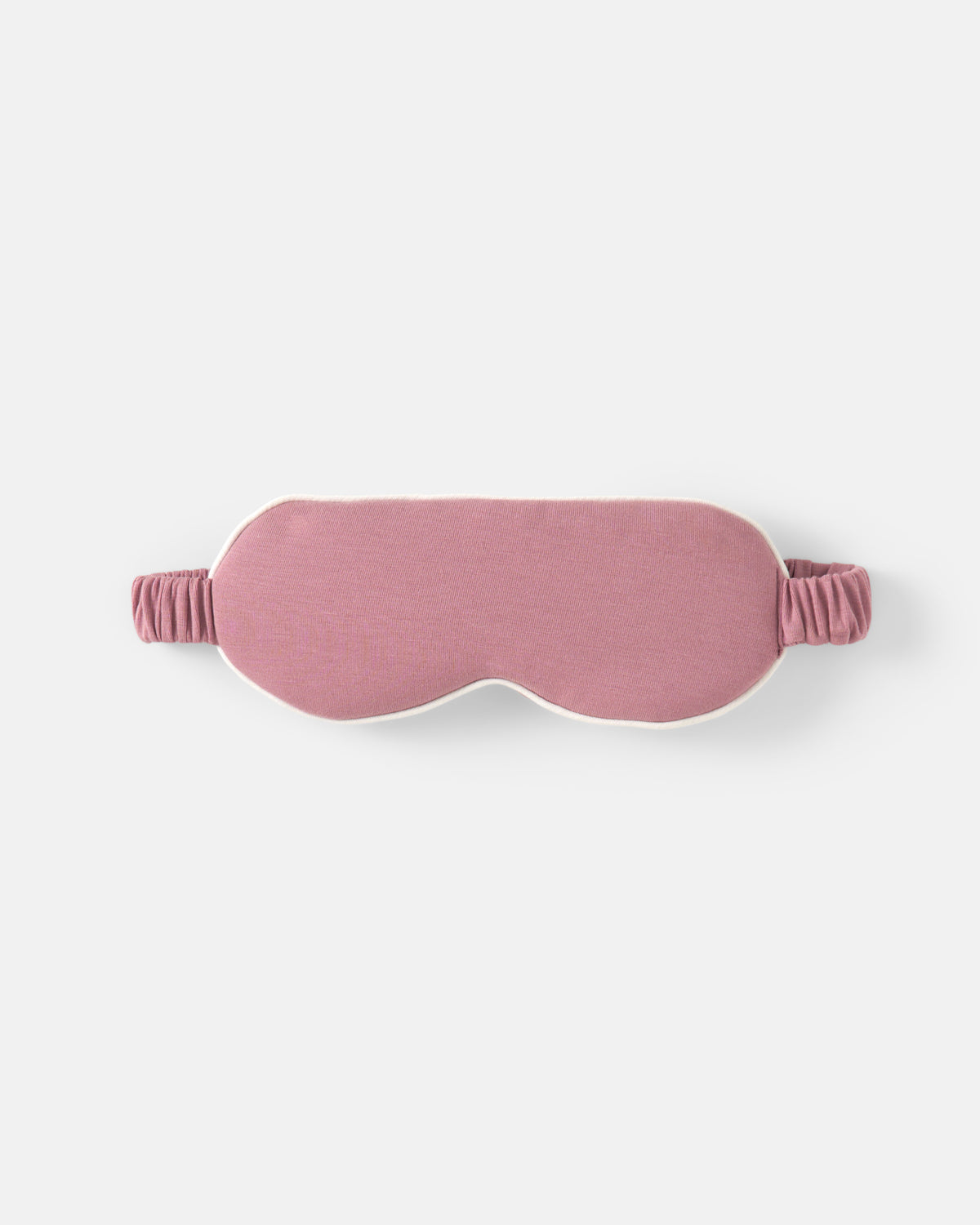 A dusty pink fabric sleep mask with an elastic strap, shown flat against a light gray background.