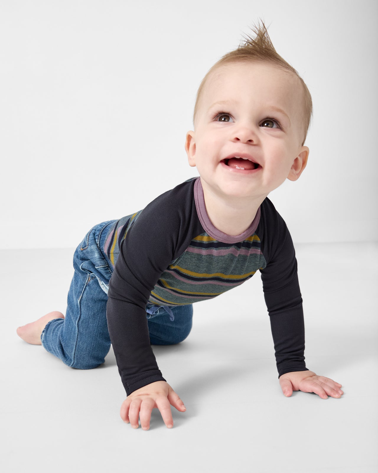 Crawling child wearing the Ollie Stripe Raglan Bodysuit with denim pants