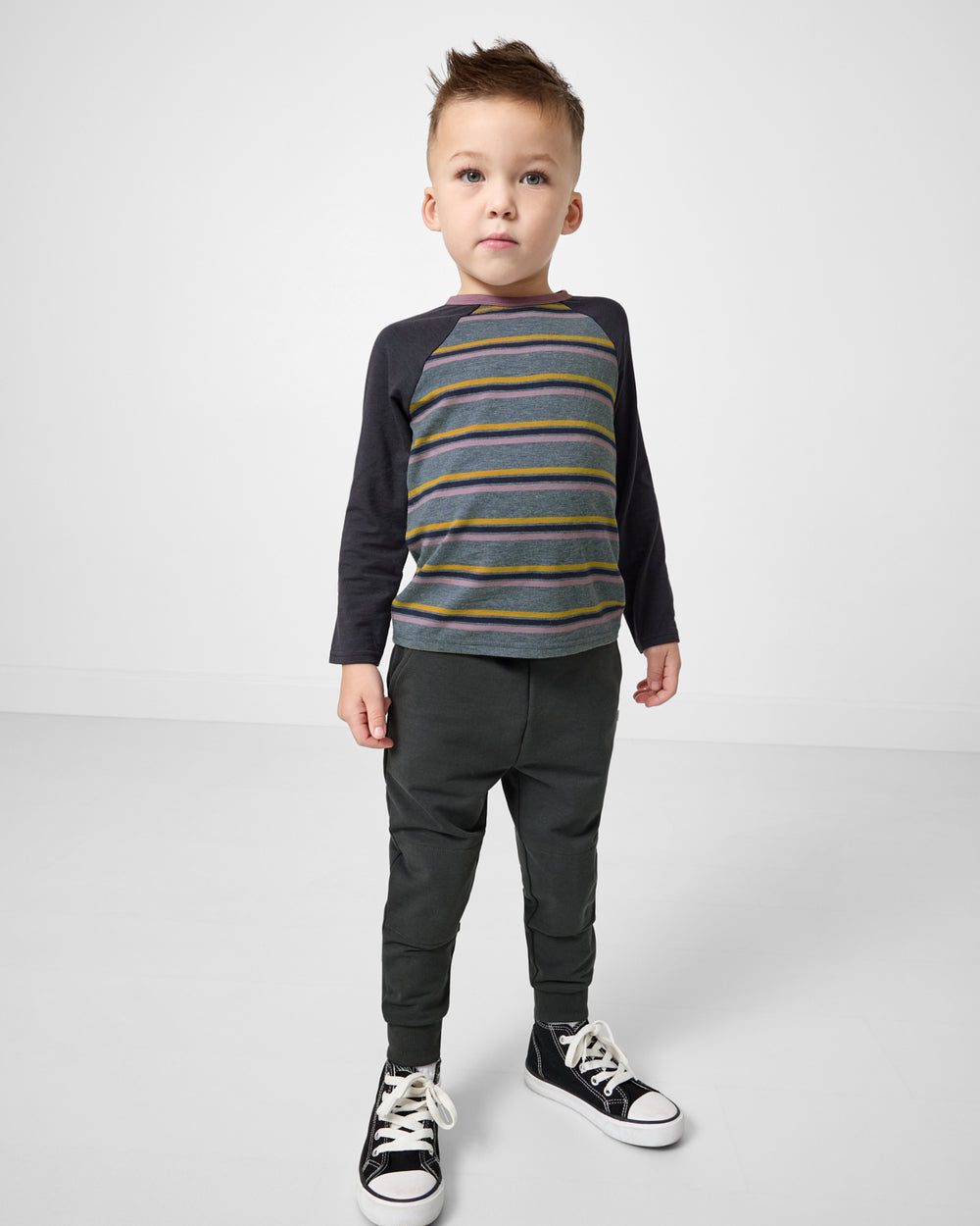 Boy wearing the Ollie Stripe Raglan Tee with gray joggers