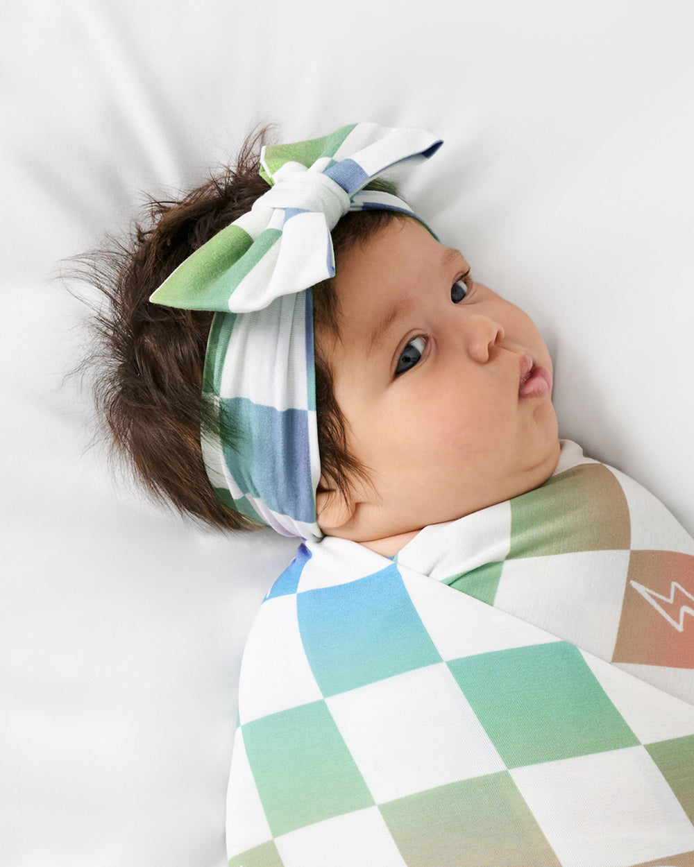 Clothes up of baby wrapped in the Ombre Cheery Checks Swaddle & Luxe Bow Headband Set