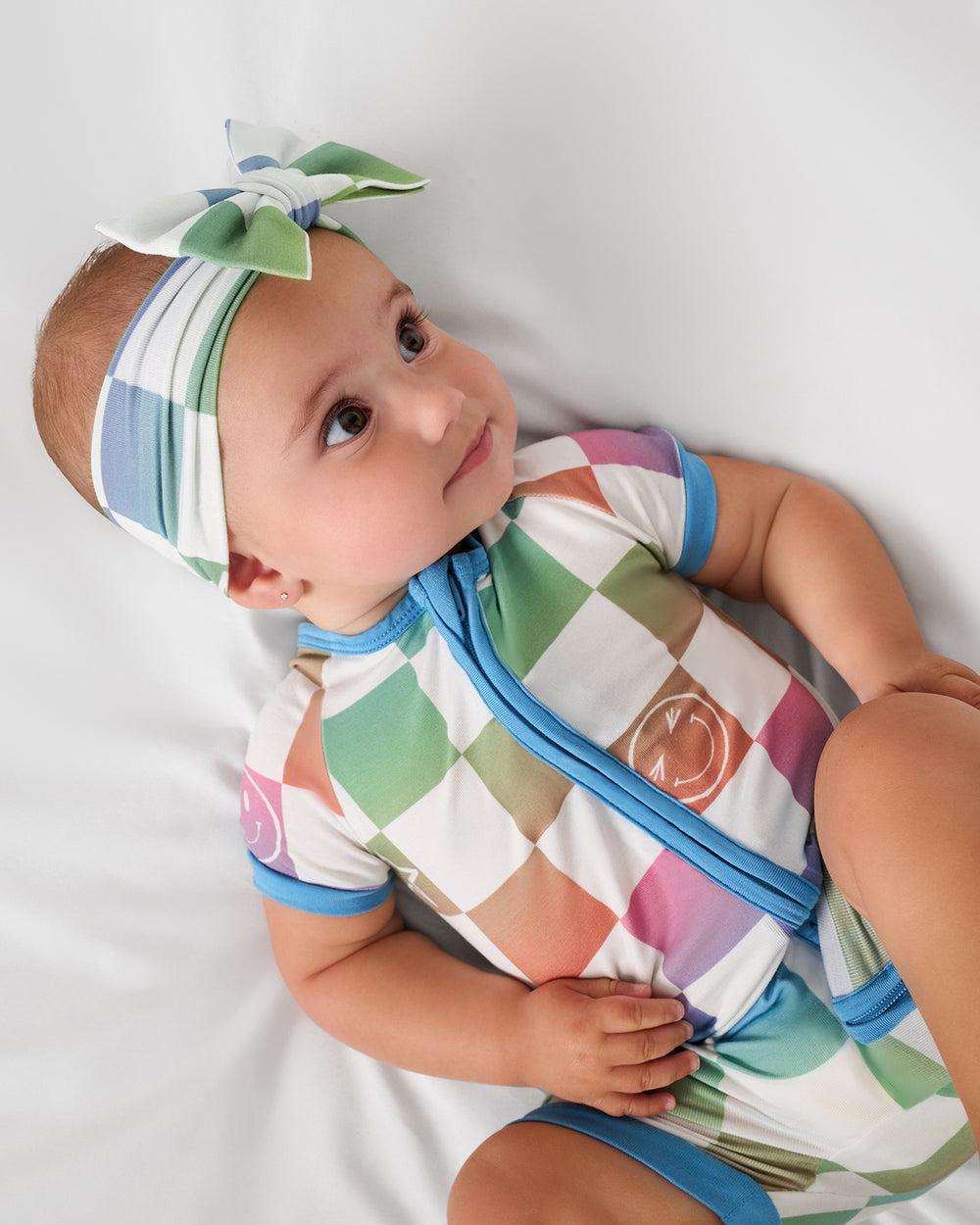 Aerial view of baby wearing the Ombre Cheery Checks Shorty Zippy on a white bed