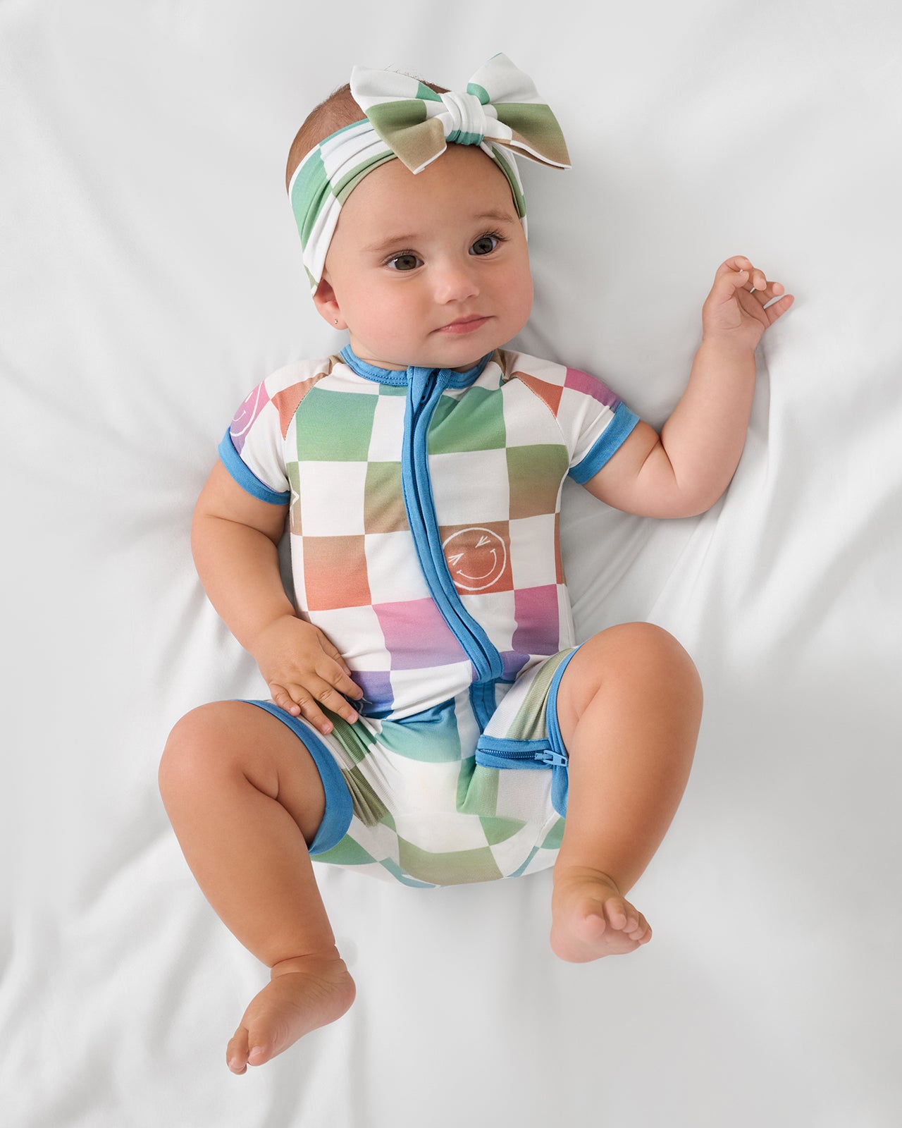 Aerial view of baby wearing the Ombre Cheery Checks Shorty Zippy and luxe bow headband