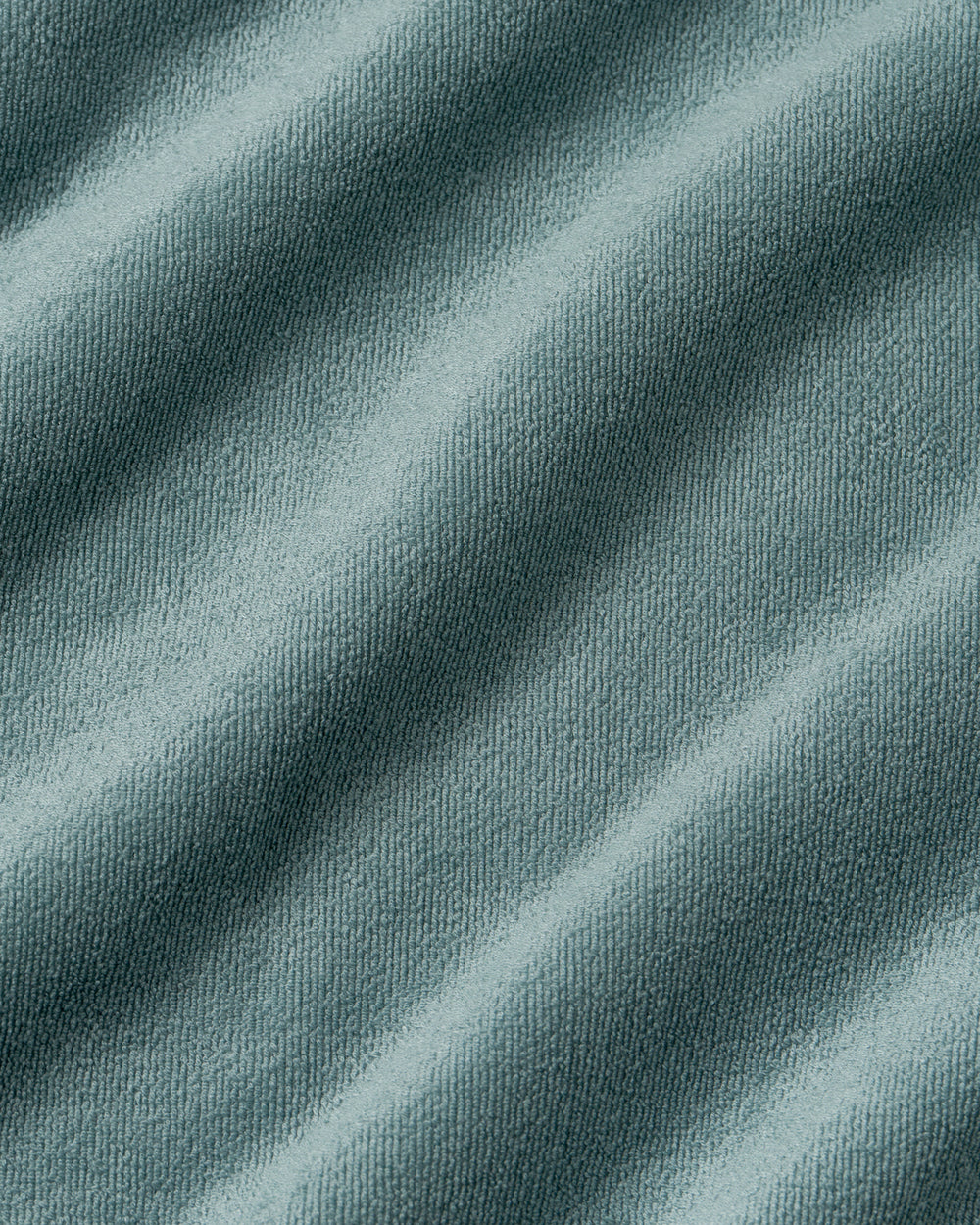 A close-up of draped slate blue-gray fabric with a fine knit texture and soft diagonal folds.