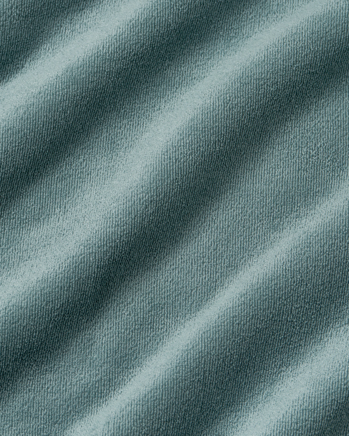A close-up of draped slate blue-gray fabric with a fine knit texture and soft diagonal folds.