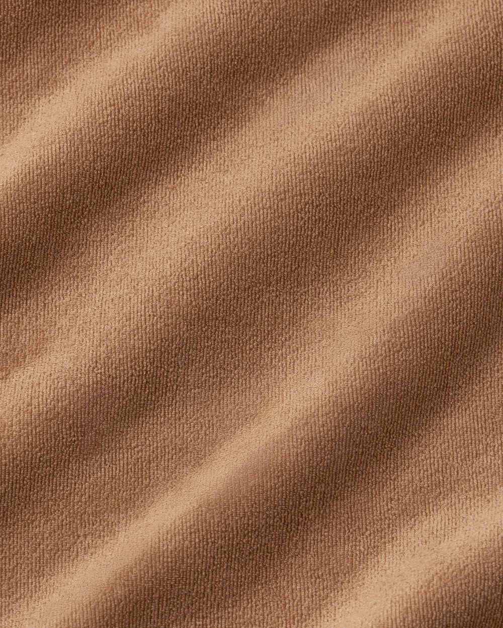 A close-up of draped brown fabric with soft folds and a fine woven texture.