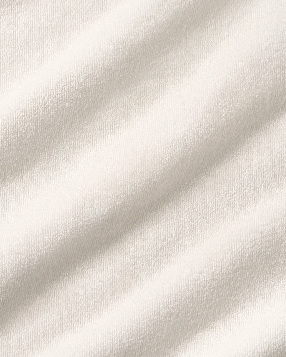 A close-up of a soft off-white fabric with a fine towel texture and gentle diagonal folds.