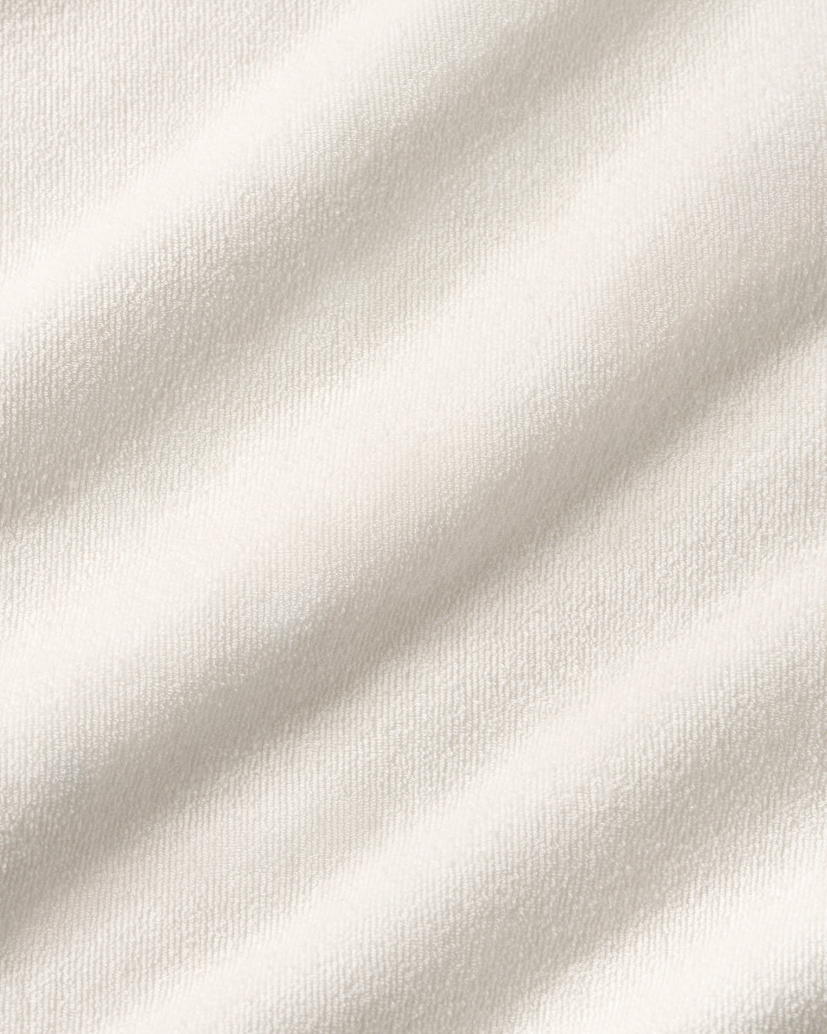 A close-up of a soft off-white fabric with a fine towel texture and gentle diagonal folds.