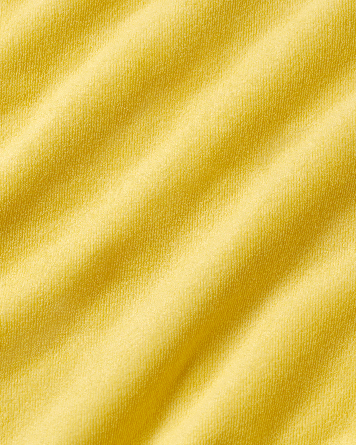 A close-up of soft yellow fabric with gentle folds and a smooth, slightly textured surface.