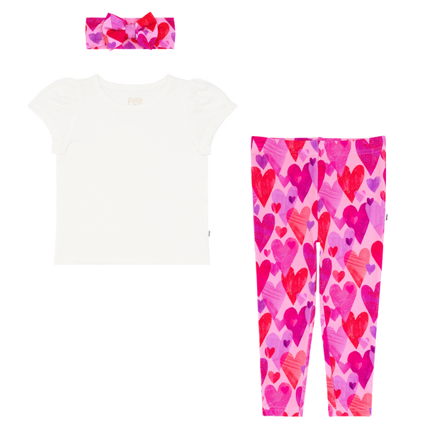 flat lay composite of a soft white puff sleeve tee and pink hearts & crafts legging and luxe bow headband