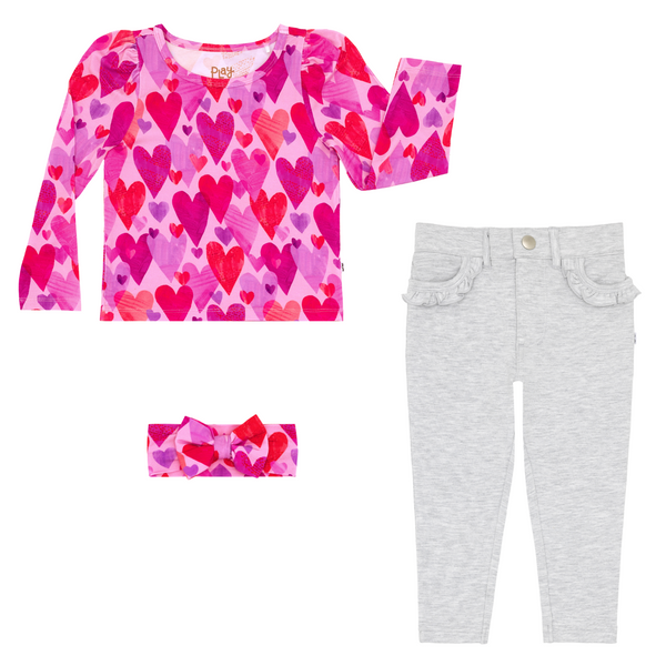 flat lay composite of a pink hearts & crafts puff sleeve tee, luxe bow headband, and light heather gray ruffle heart pocket pants