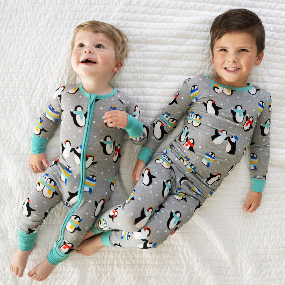 two children laying on a bed wearing matching Penguin Party pjs in zippy and two piece styles