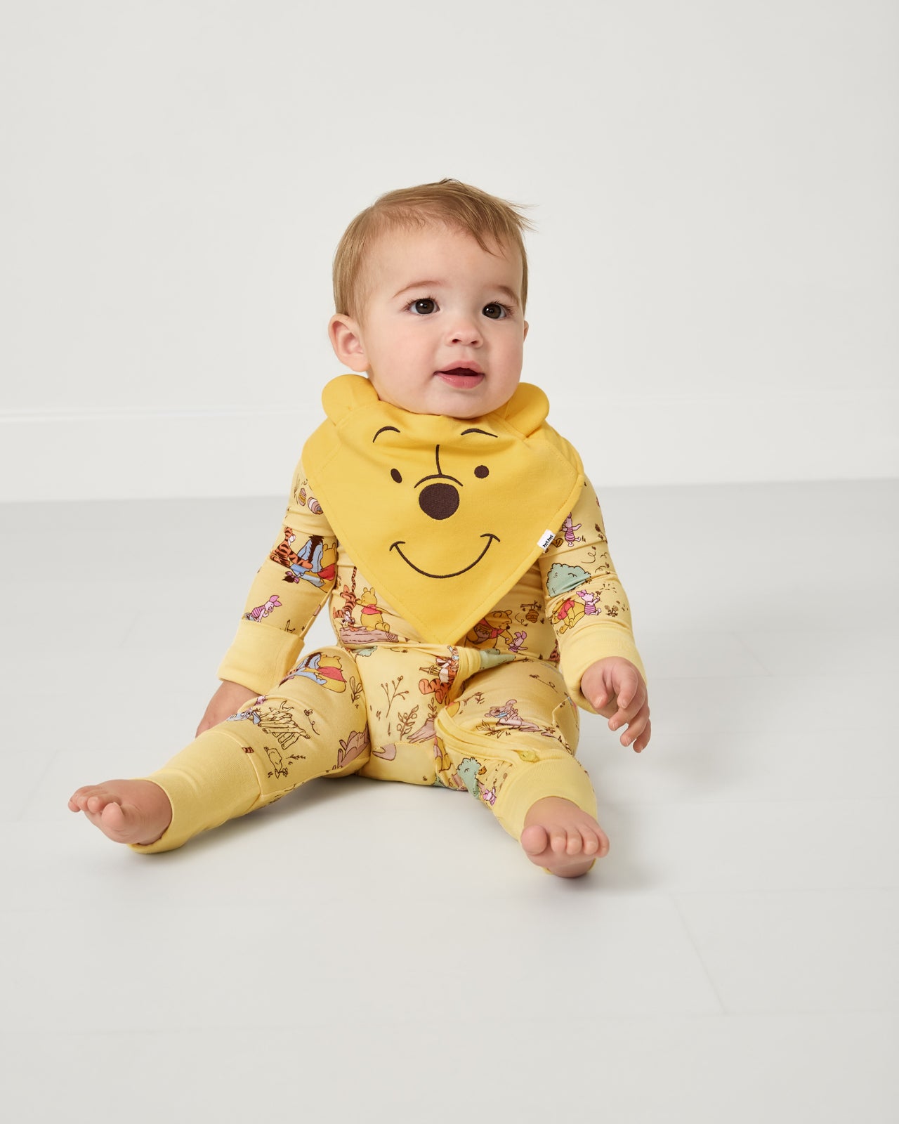 Sitting baby wearing the Disney Winnie The Pooh Bandana Bib and matching zipper pajamas