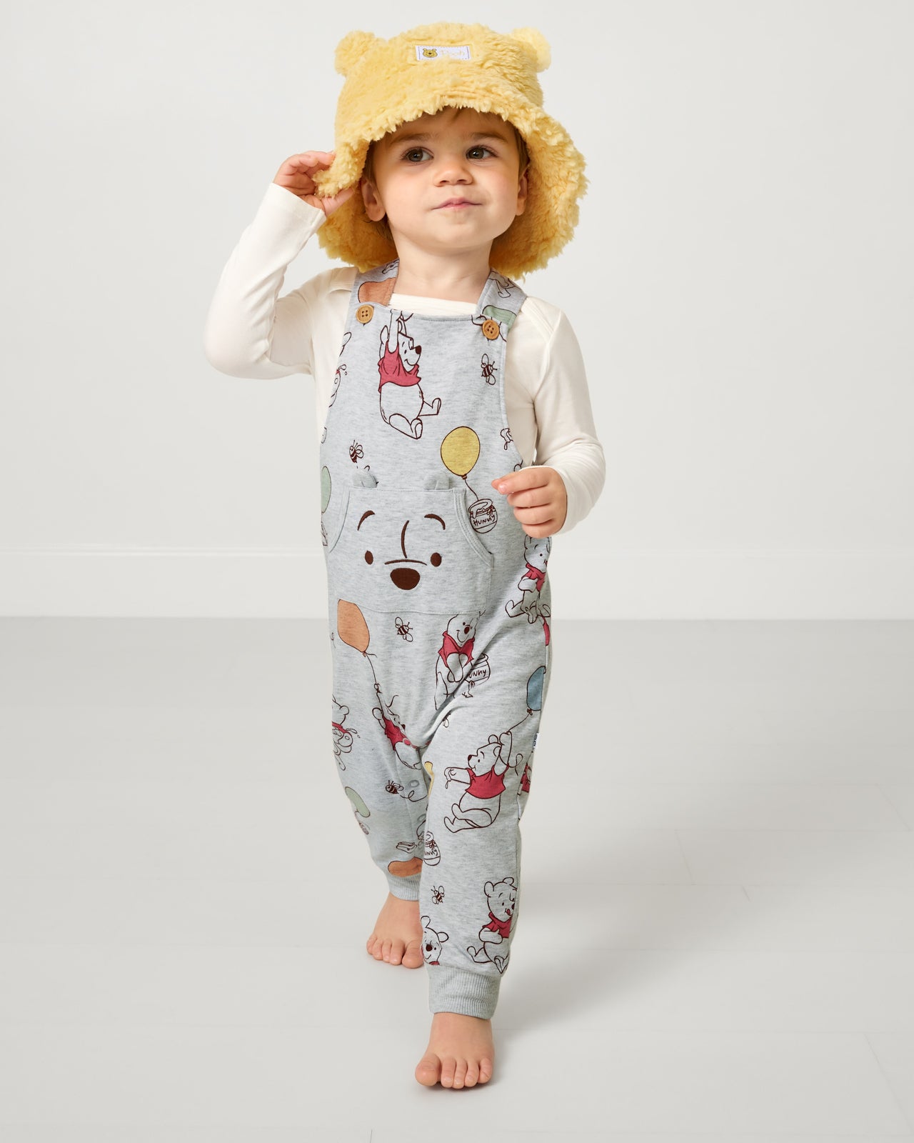 Toddler wearing the Disney Winnie the Pooh Sherpa Bucket Hat with Pooh themed overalls