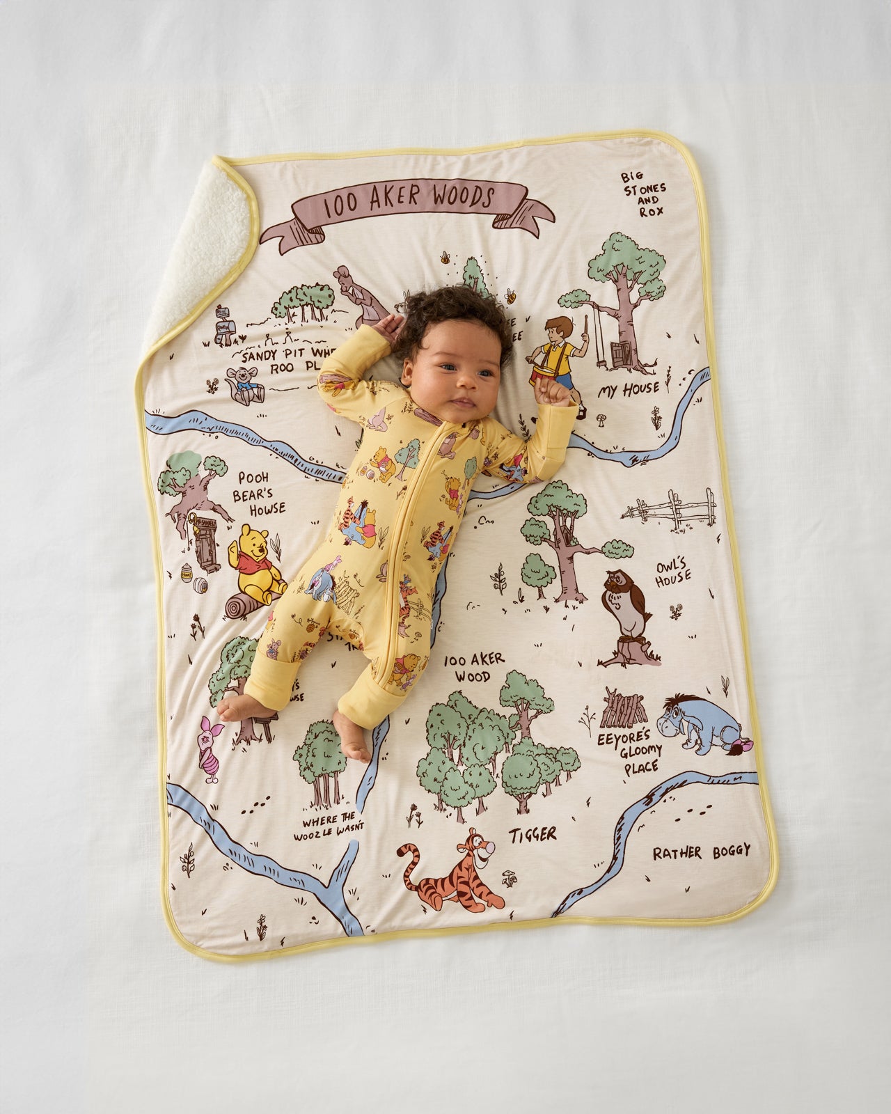 Aerial view of baby wearing the Disney Playtime With Pooh Zippy on a 100 Aker Woods blanket