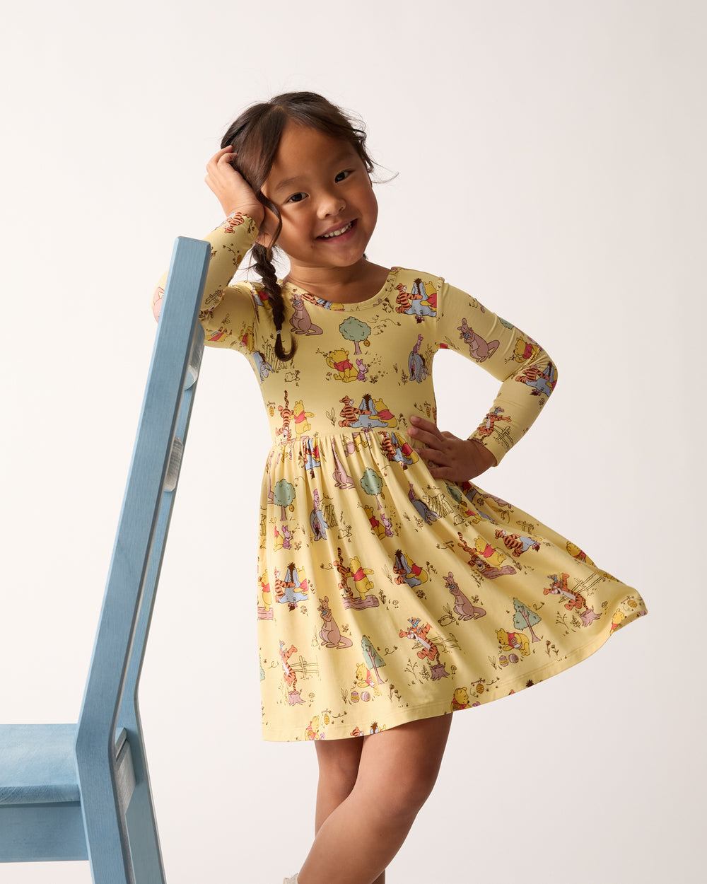 Girl leaning on a chair wearing the Disney Playtime With Pooh Skater Dress