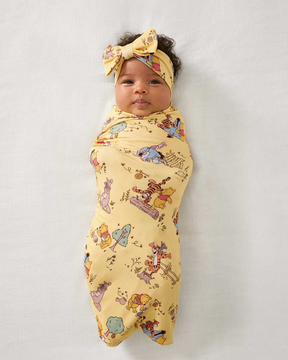 Aerial view of baby wearing the Disney Playtime With Pooh Swaddle & Luxe Bow Headband Set
