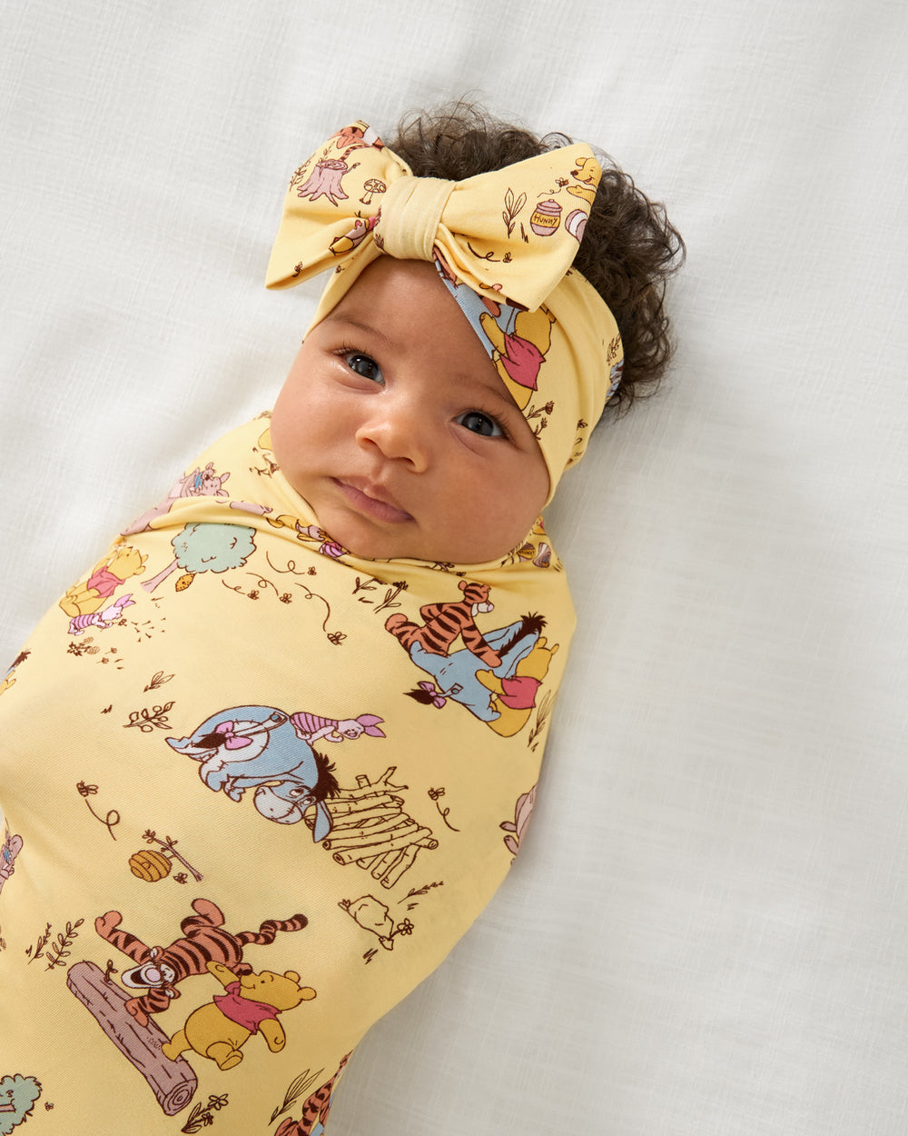 Close up of baby wrapped in the Disney Playtime With Pooh Swaddle & Luxe Bow Headband Set