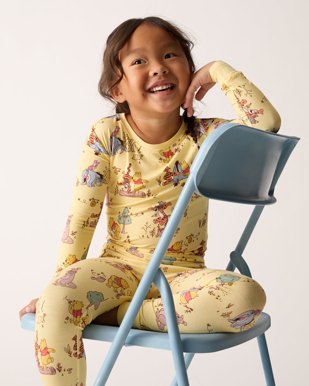 Girl sitting on a chair wearing the Disney Playtime With Pooh Two-Piece Pajama Set 