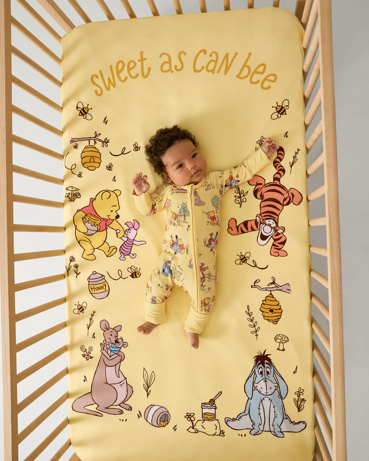 Aerial view baby laying in a crib with the Disney Sweet As Can Bee Fitted Crib Sheet