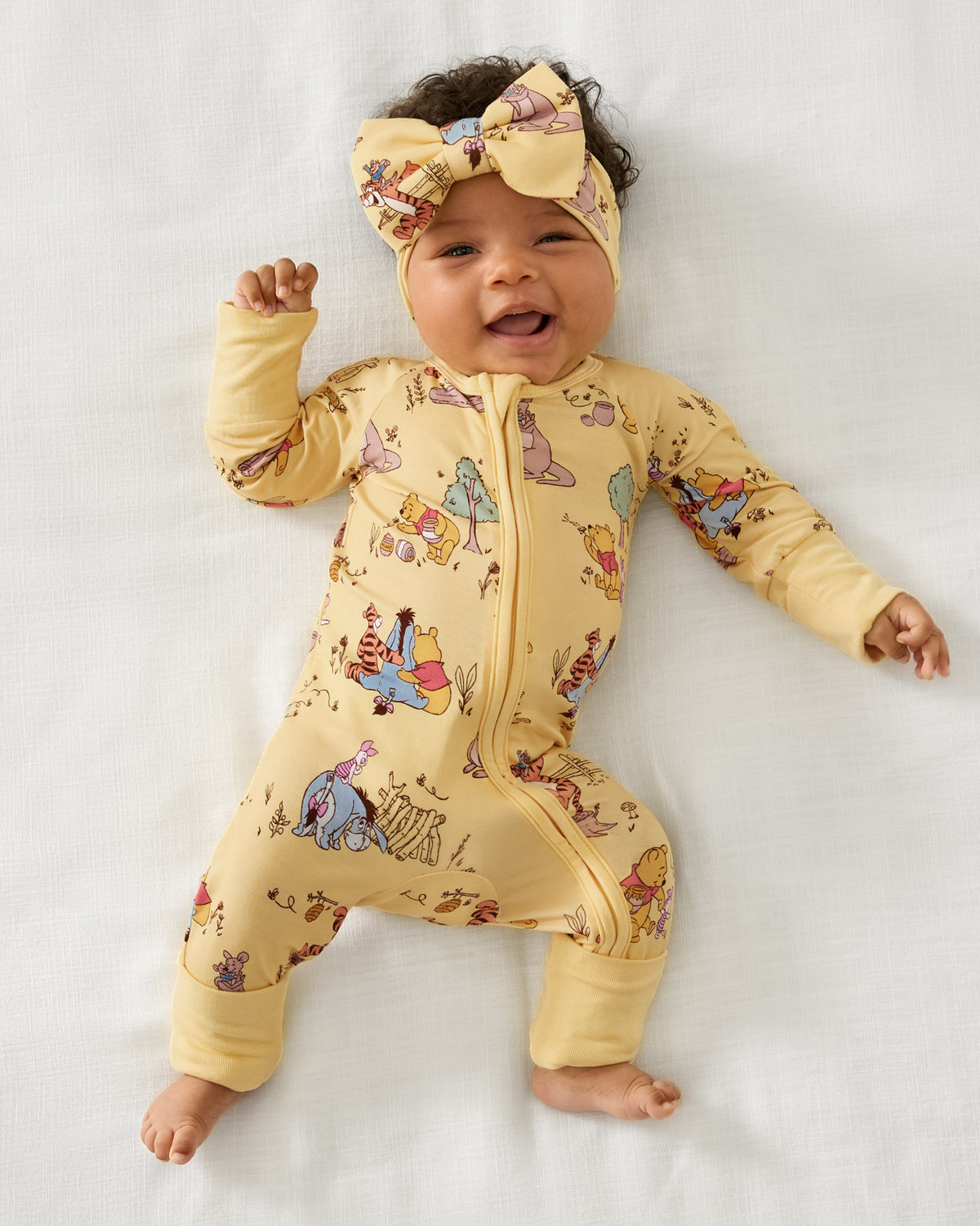 Alternate aerial view of baby wearing the Disney Playtime With Pooh Zippy and matching bow headband