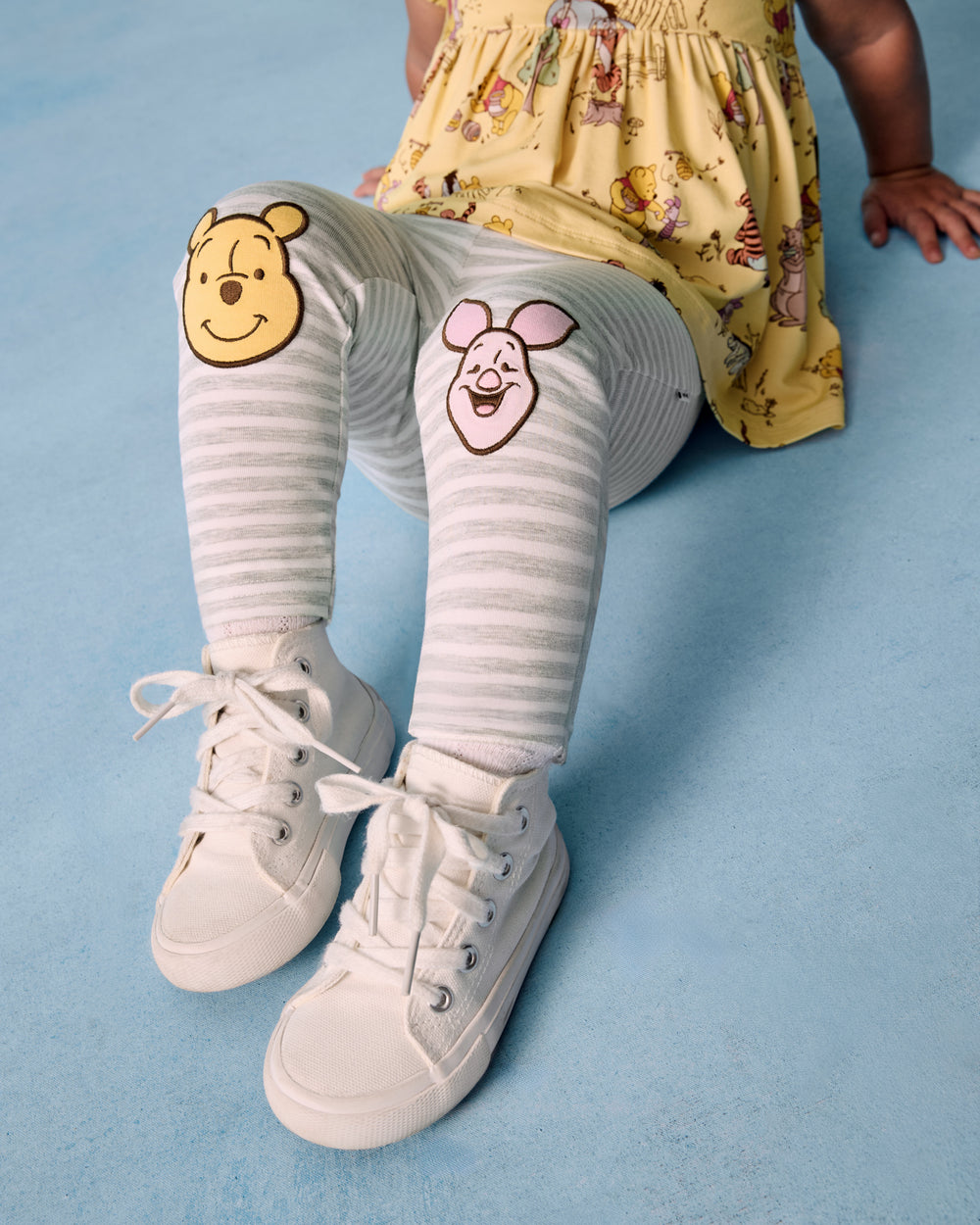 Sitting child wearing the Disney Winnie The Pooh Patch Legging on a blue background