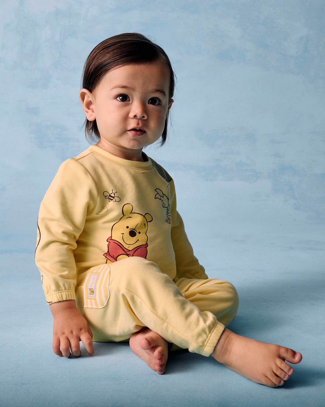 Sitting child wearing the Disney Winnie The Pooh Cinched Jogger on a blue background
