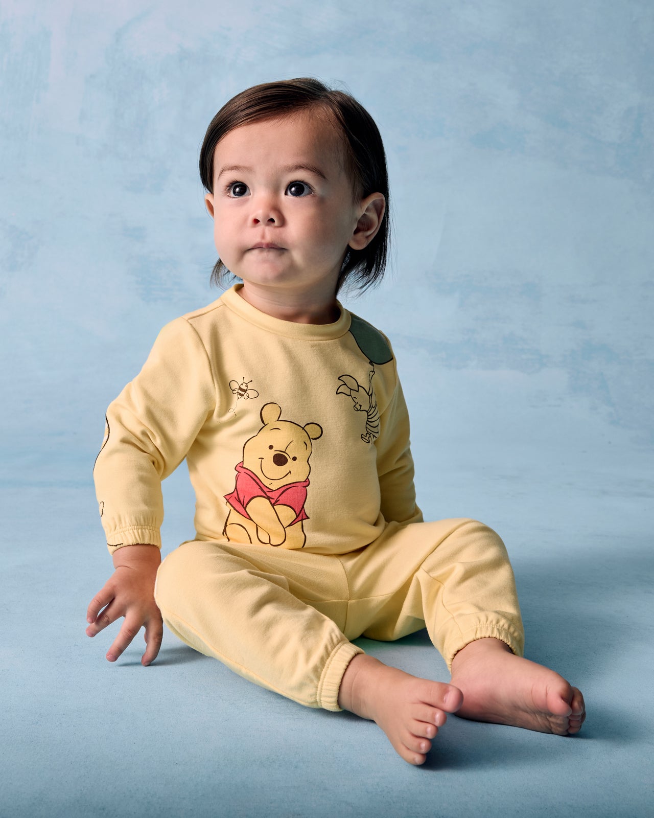 Sitting child wearing the Disney Winnie The Pooh Cinched Crewneck and Joggers on a blue background