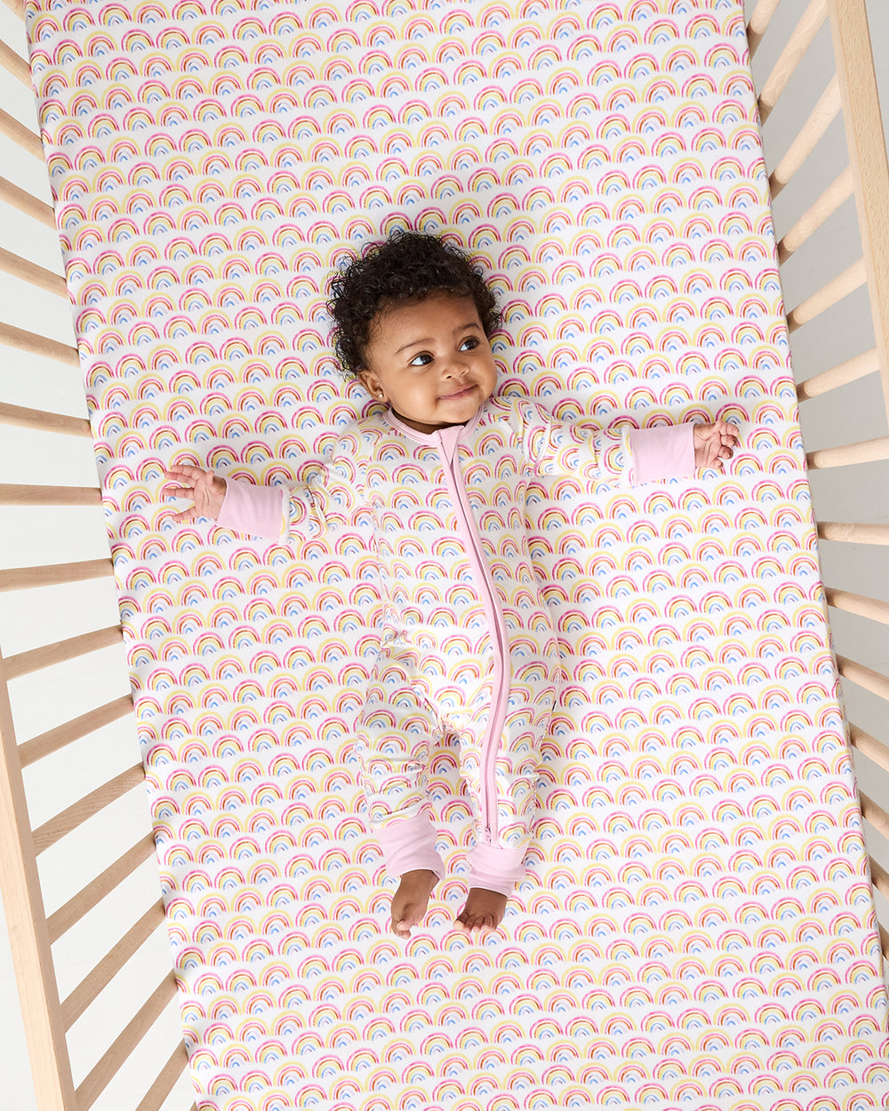 Overhead view of baby laying on the Pastel Rainbows Fitted Crib Sheet