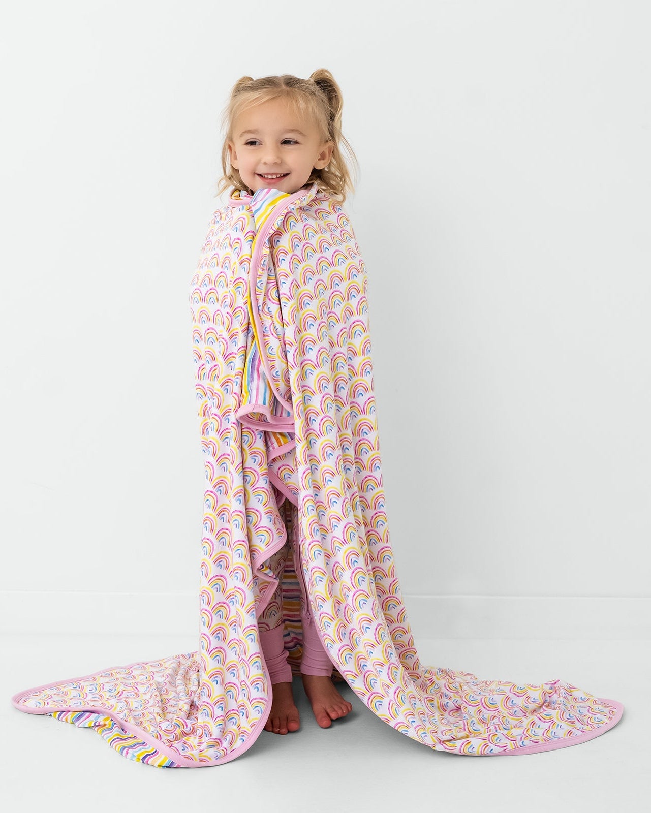 Standing child wrapped in the Pastel Rainbows & Sunrise Stripes Large Cloud Blanket®