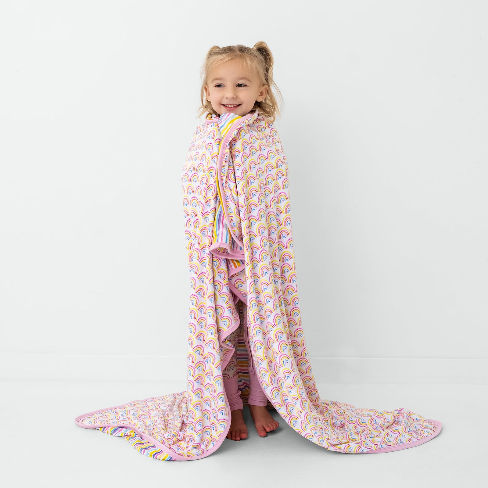 Standing child wrapped in the Pastel Rainbows & Sunrise Stripes Large Cloud Blanket®