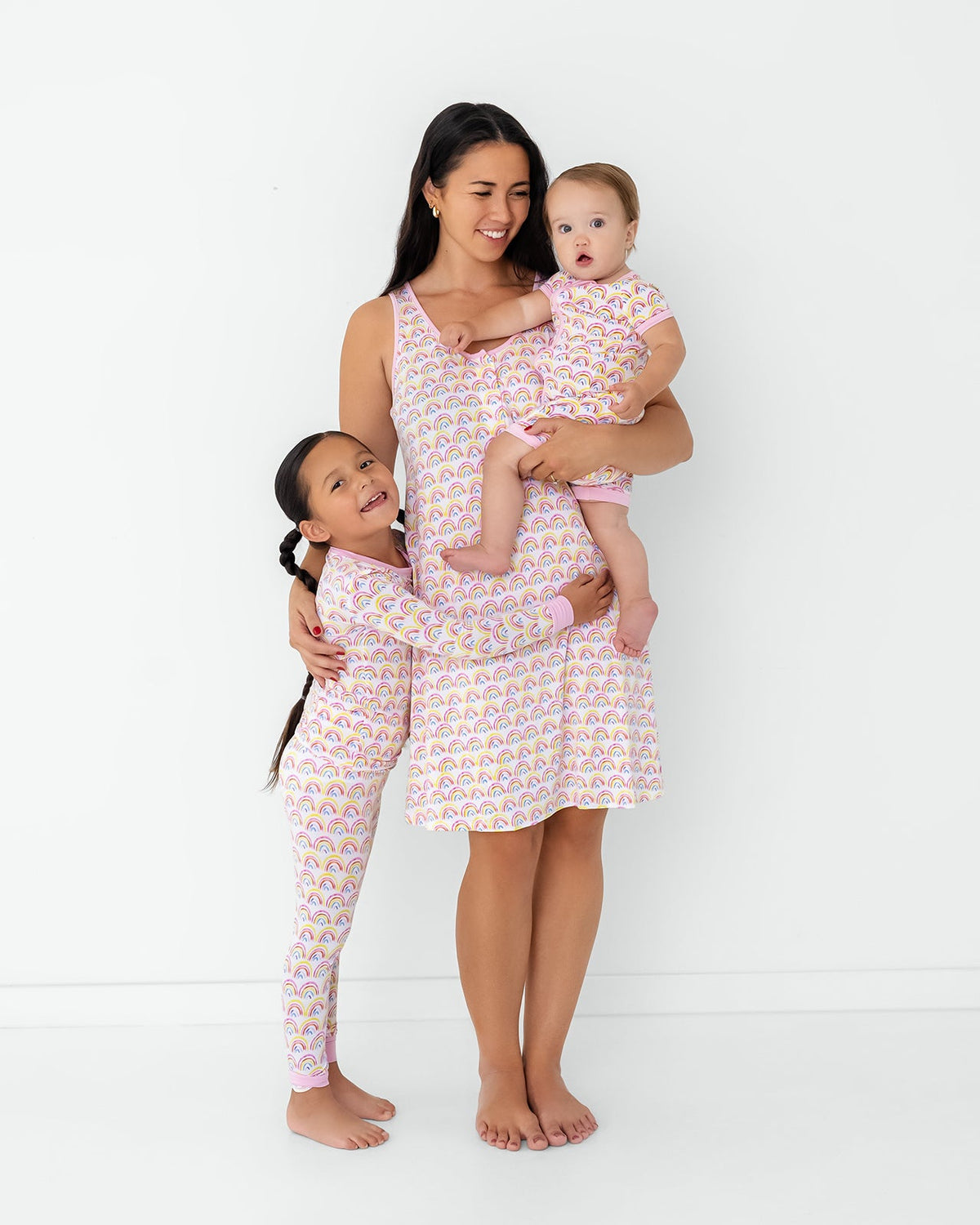Standing mother and two children wearing matching Pastel Rainbows pajamas