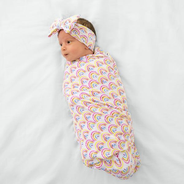 Aerial view of child wearing the Pastel Rainbows Swaddle & Luxe Bow Headband Set