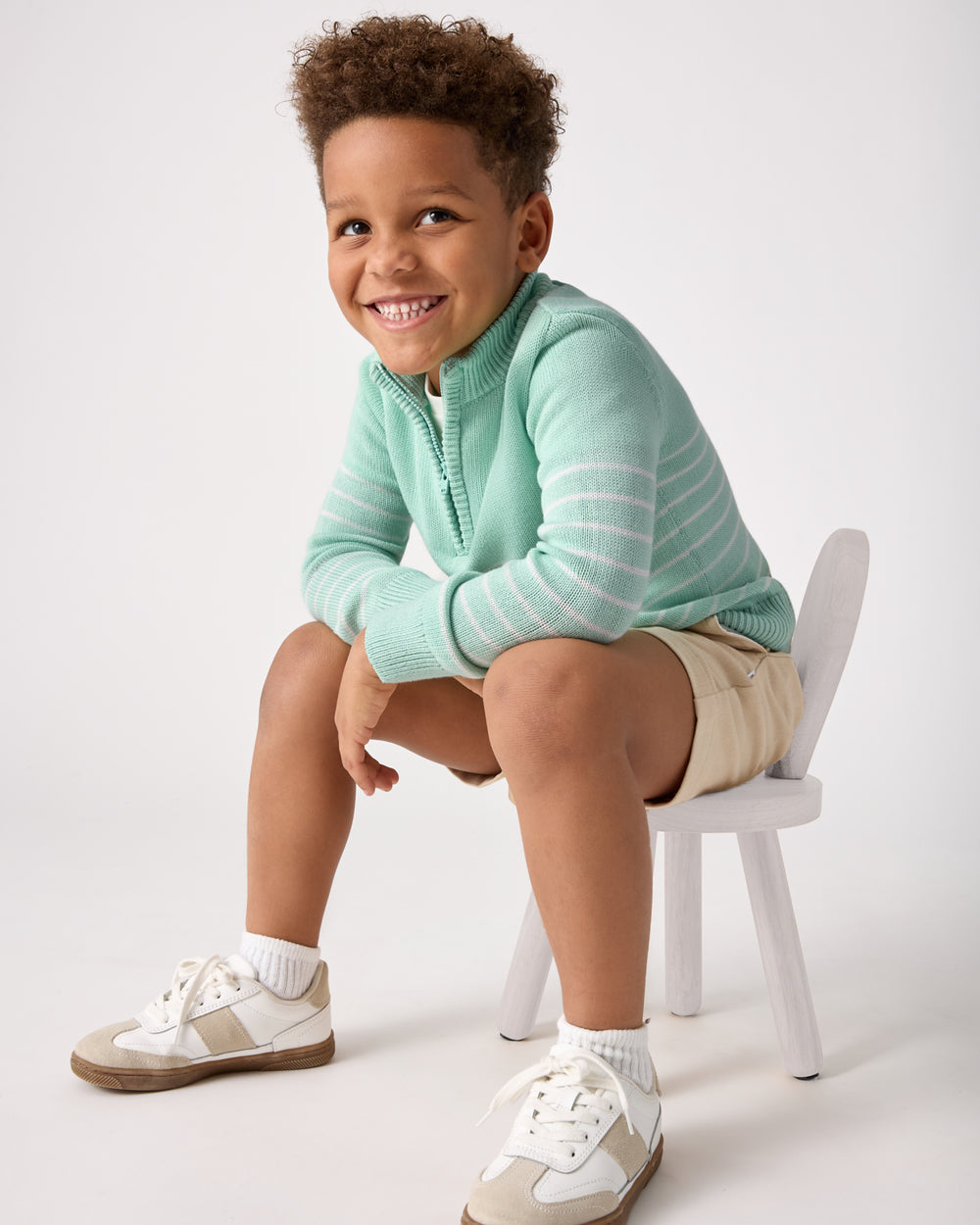 Boy sitting on a chair wearing the Pastel Green Stripe Zip Sweater
