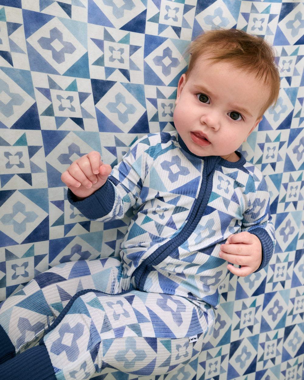 Baby laying on the Patchwork Indigo Fitted Crib Sheet wearing the coordinating zippy