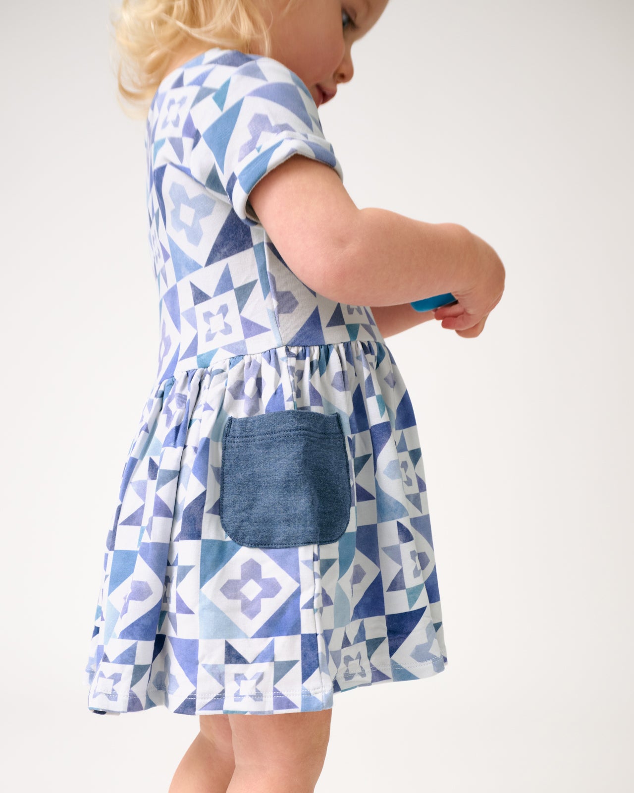 Side view of toddler wearing the Patchwork Indigo Patch Pocket Dress with Bloomer
