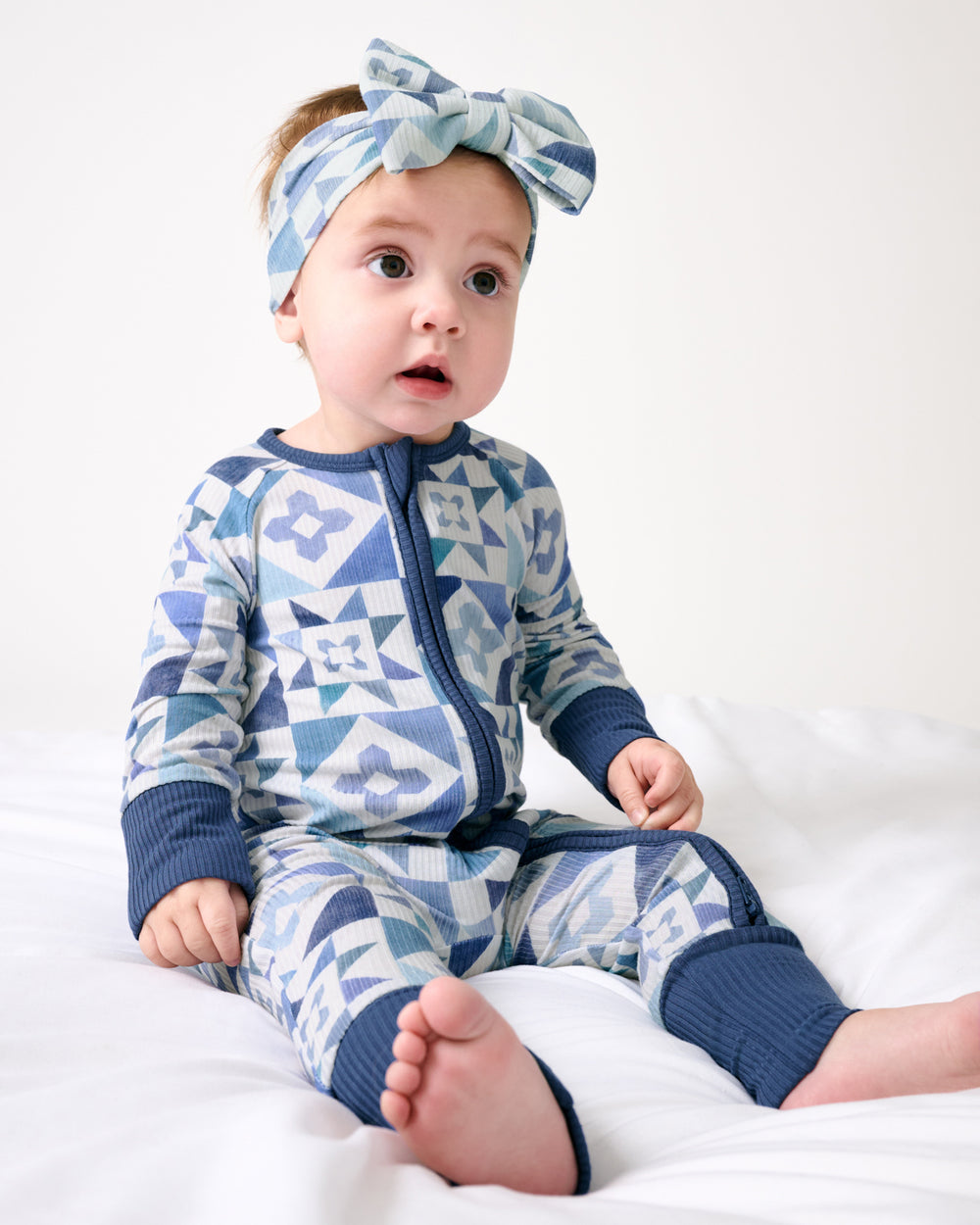 Sitting baby wearing the Patchwork Indigo Ribbed Luxe Bow Headband and Zippy