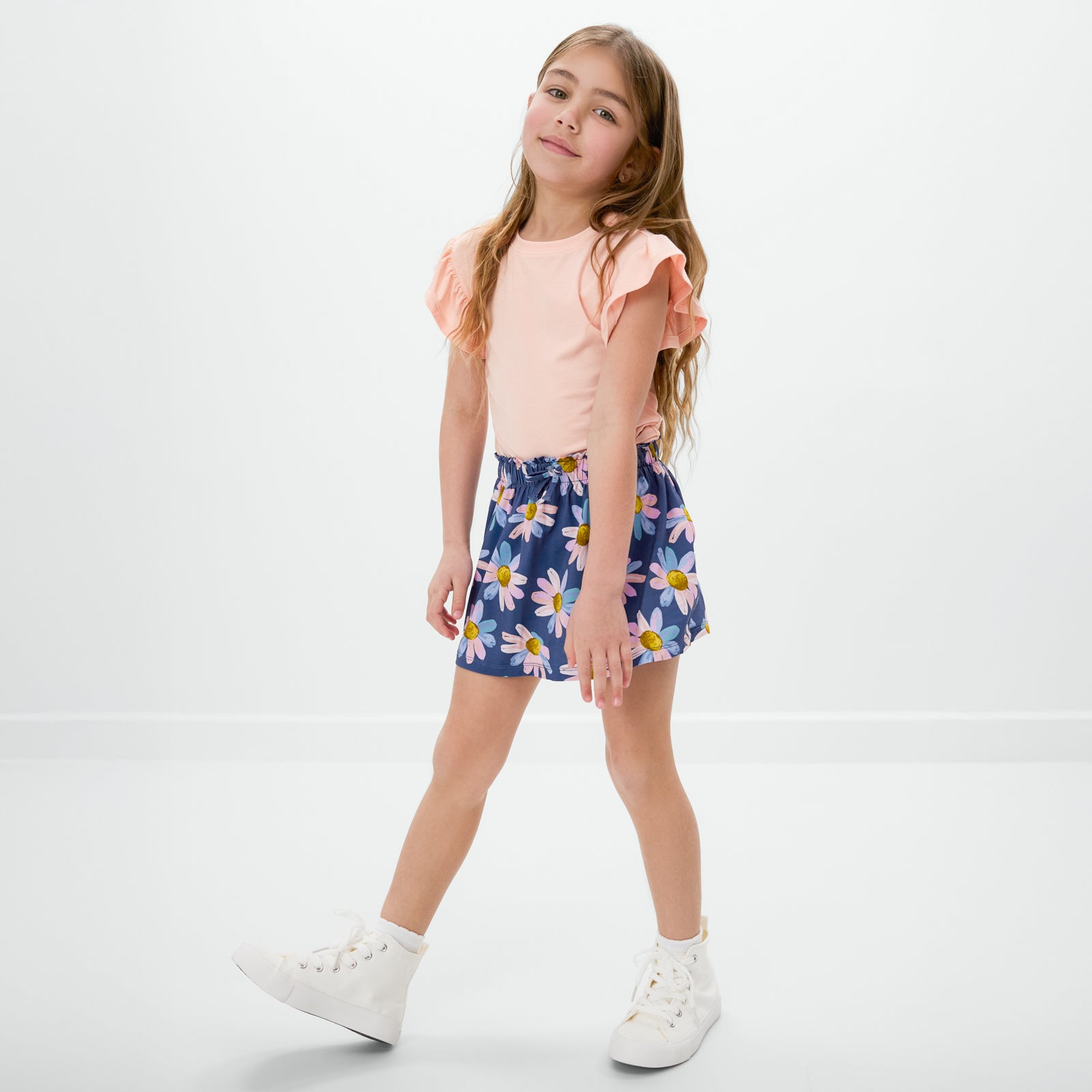 Walking child wearing the Peach Sorbet Ruffle Tee with the Daisy Blooms skort