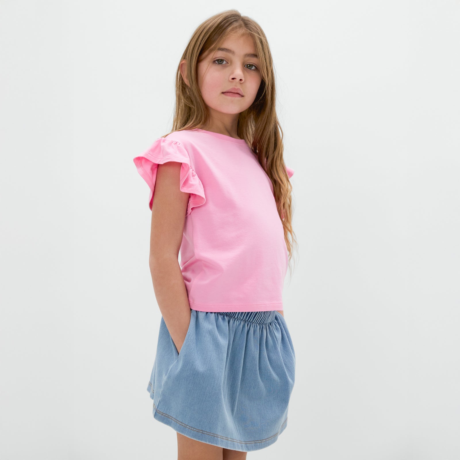 Standing child wearing the Light Blue Denim Skort with the Peppy Pink flutter tee